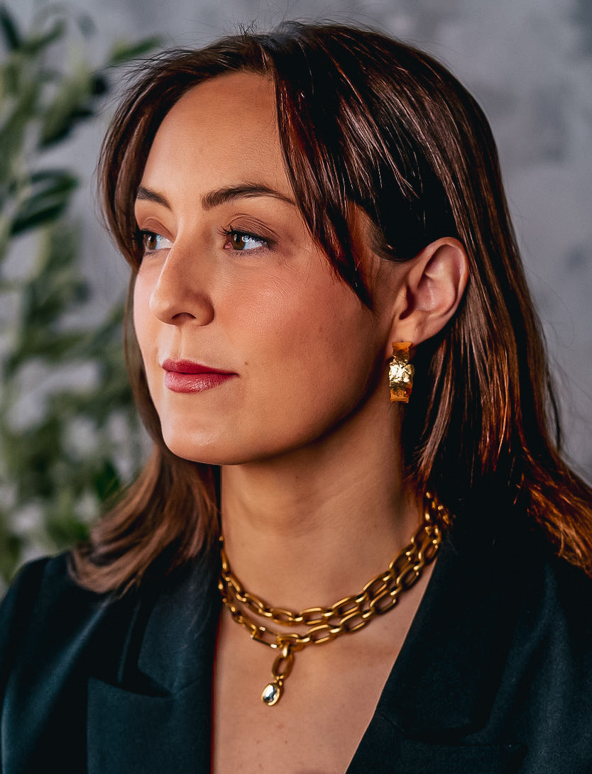 a model wearing a large hammered gold hoop earring.