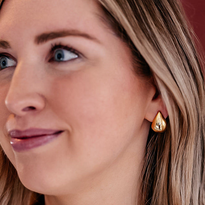A model wearing A pair of gold teardrop earrings.