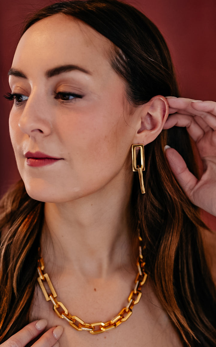 A model wearing A gold dangle earring with interlocking rectangle shapes.