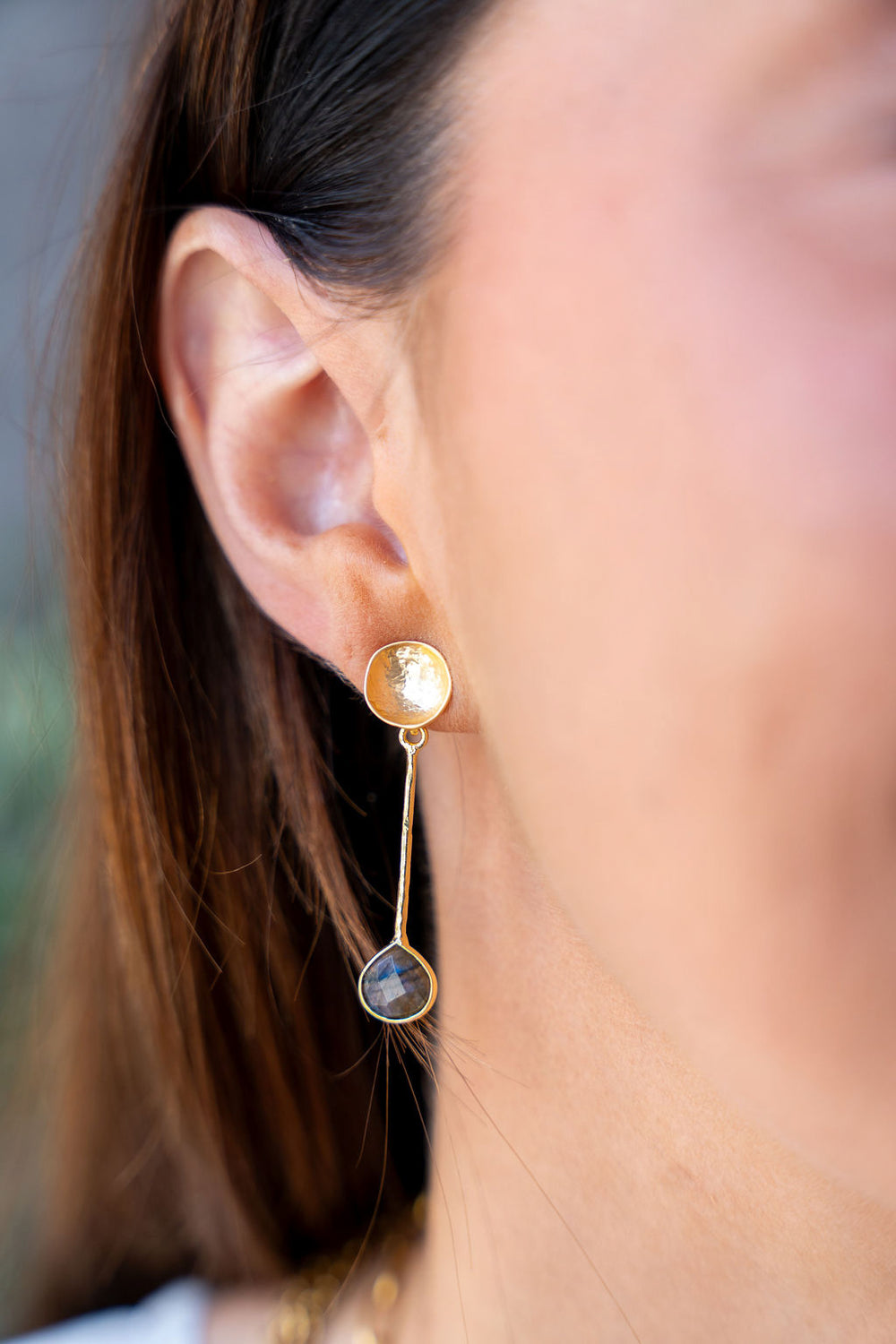Gold drop earrings with hammered disc tops, textured vertical bars, and teardrop labradorite stones at the base.