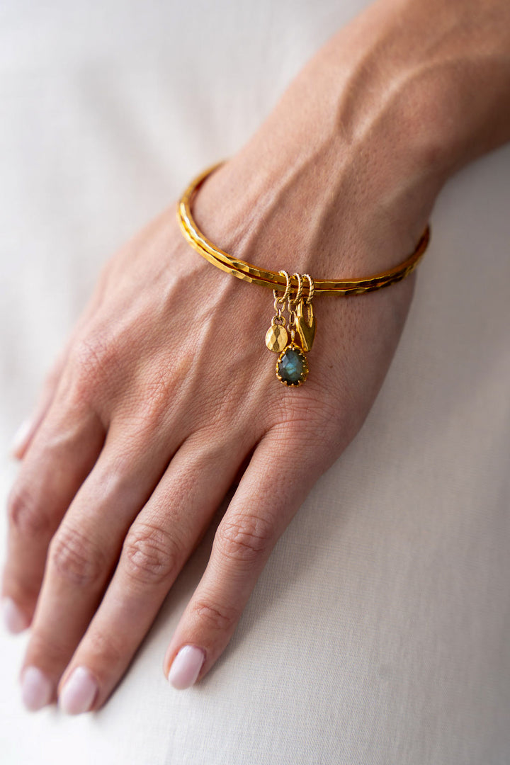 Two slim gold bangles with labradorite, heart, and gold coin charms.