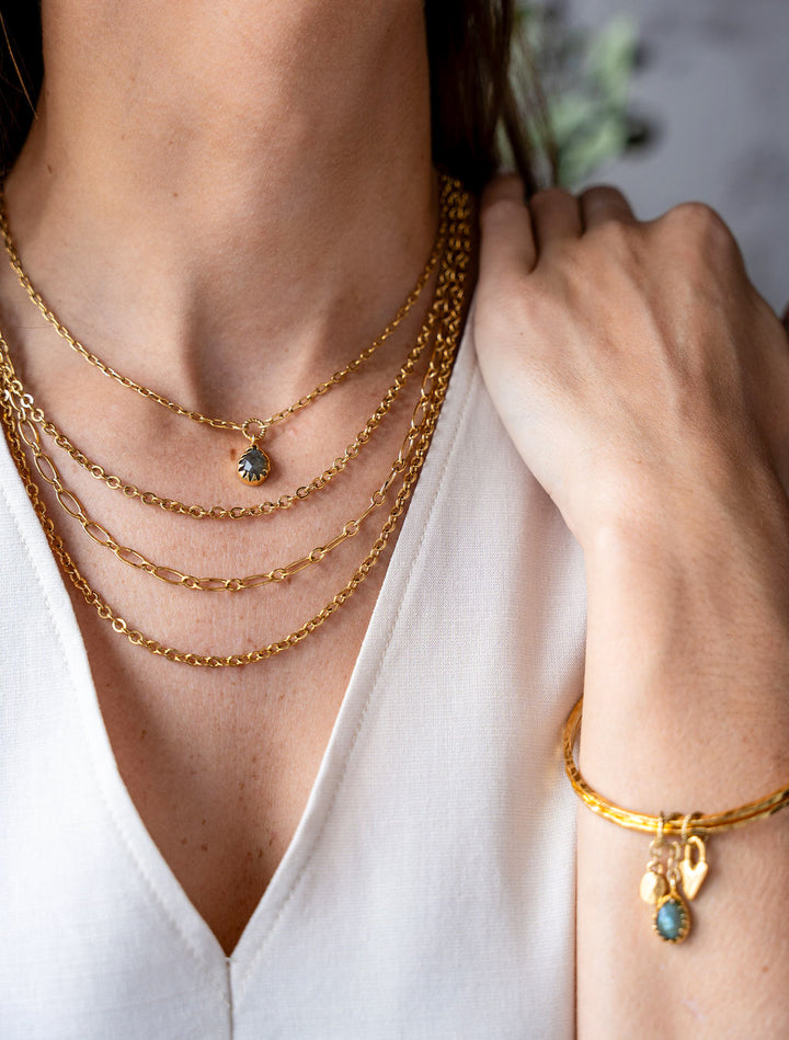 Two slim gold bangles with labradorite, heart, and gold coin charms.