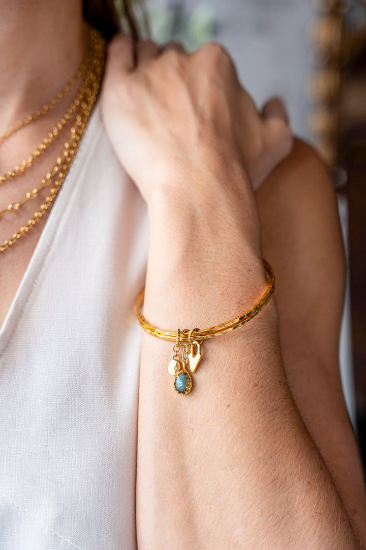 Two slim gold bangles with labradorite, heart, and gold coin charms.
