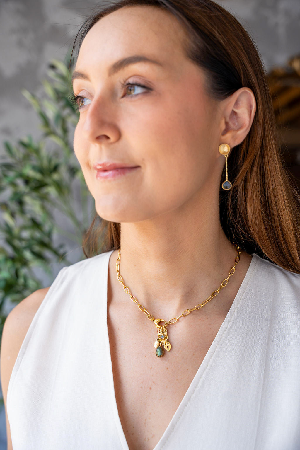 Gold chain necklace with a front clasp and dangling charms including a teardrop labradorite and textured gold talismans.