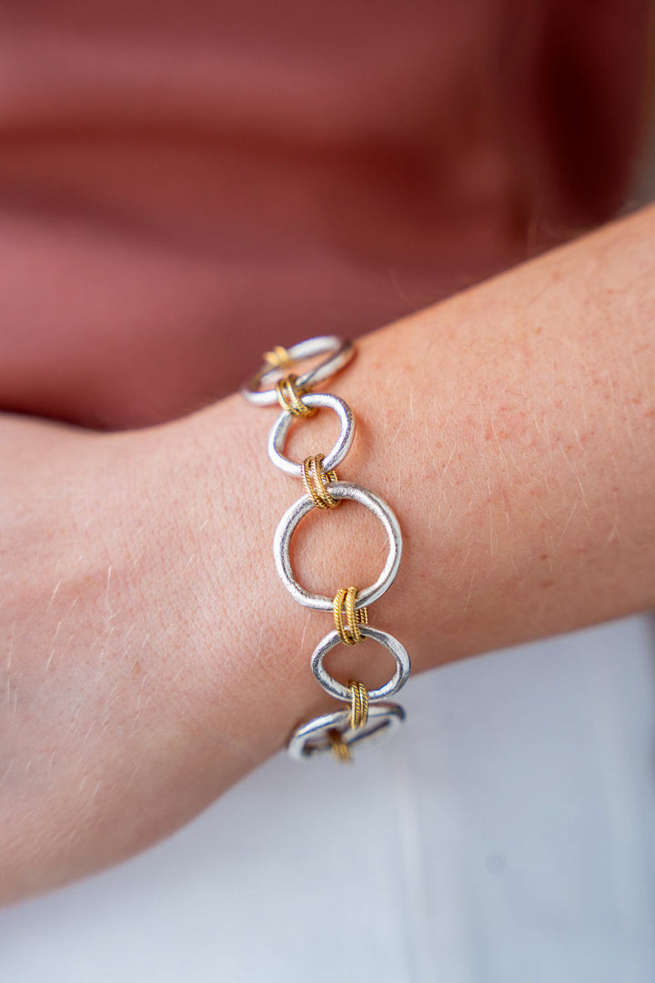 Mixed metal bracelet featuring brushed silver sculpted circle links with gold rope accents and a toggle clasp.