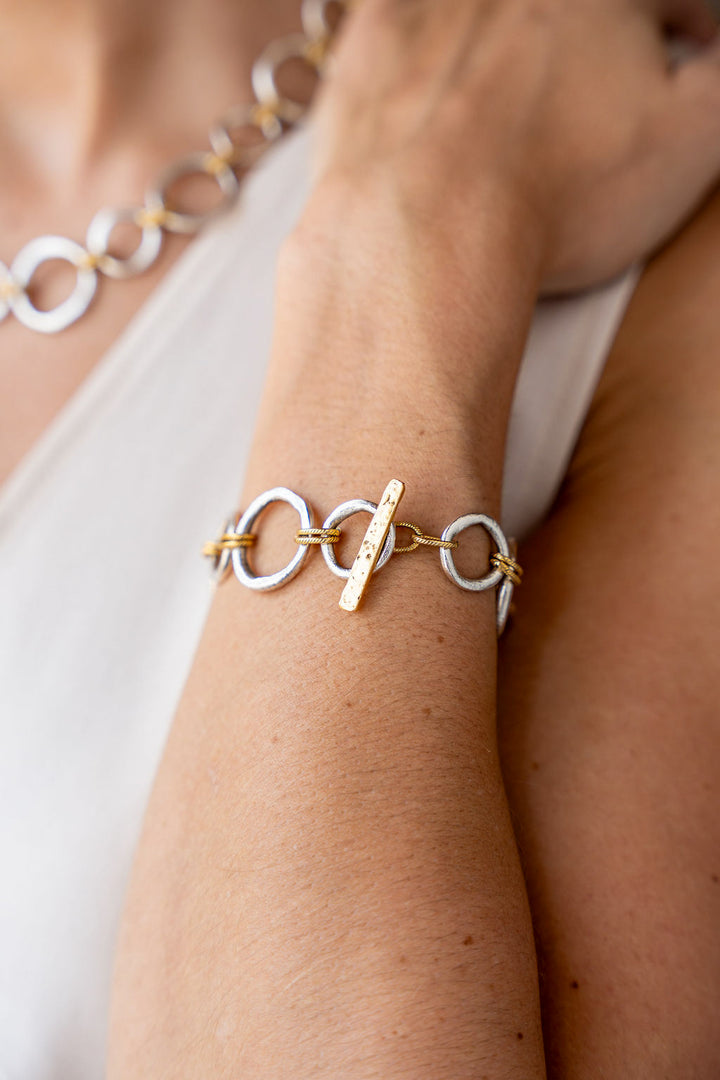 Mixed metal bracelet featuring brushed silver sculpted circle links with gold rope accents and a toggle clasp.