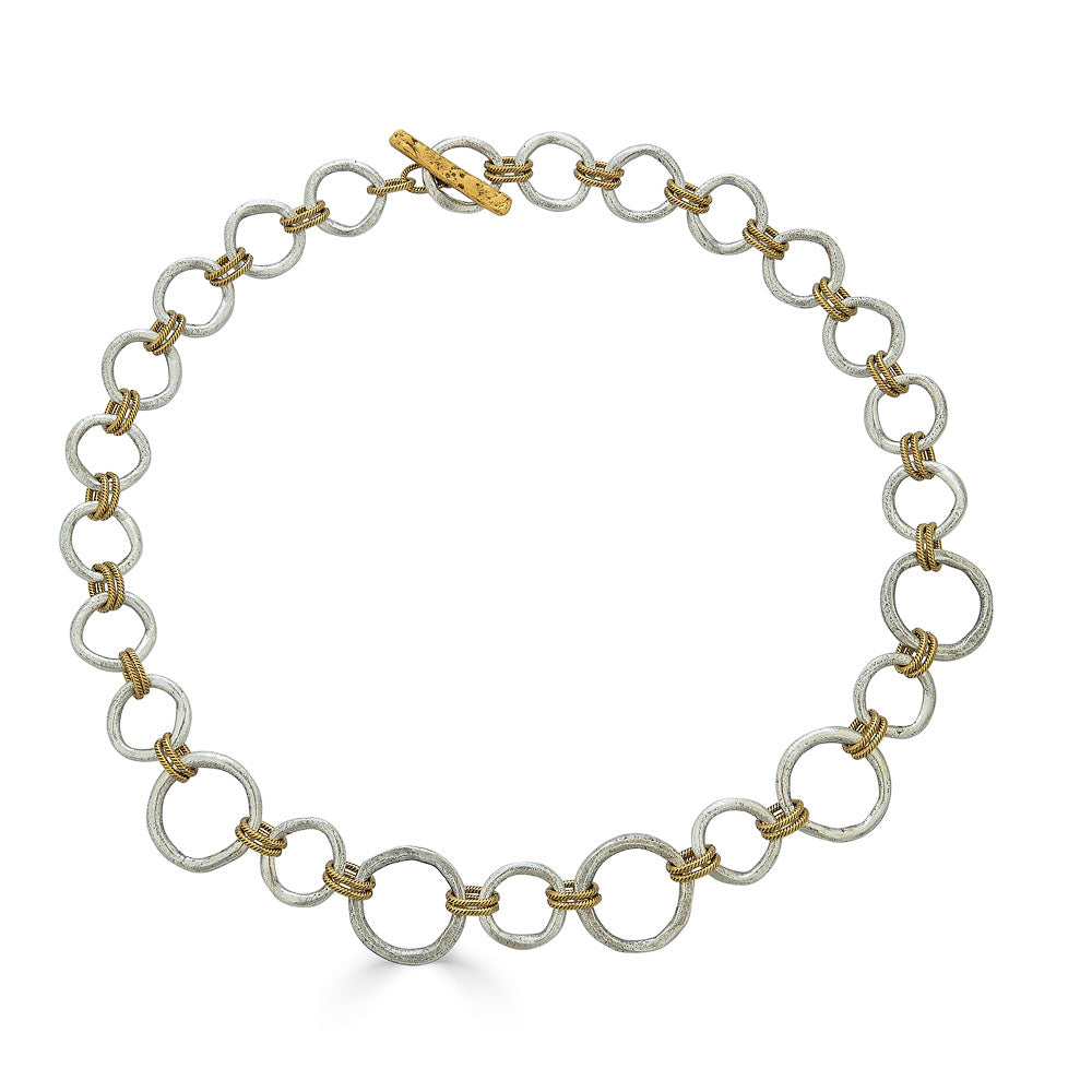Mixed metal necklace with matte silver and gold sculpted circle links, toggle clasp, and rope-textured accents styled multiple ways.