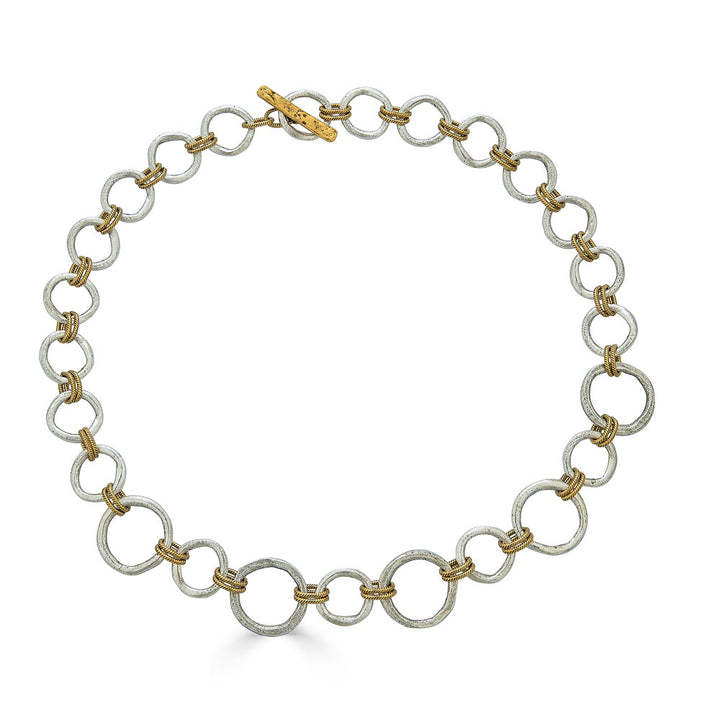 Mixed metal necklace with matte silver and gold sculpted circle links, toggle clasp, and rope-textured accents styled multiple ways.