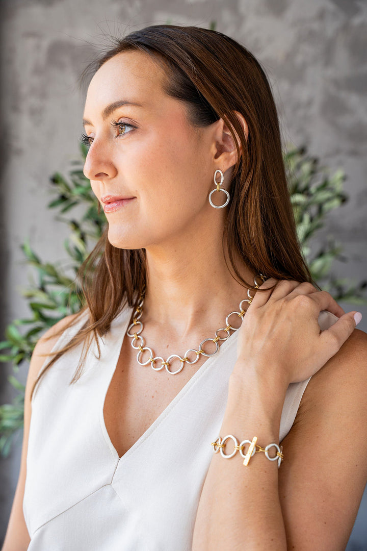 Mixed metal necklace with matte silver and gold sculpted circle links, toggle clasp, and rope-textured accents styled multiple ways.