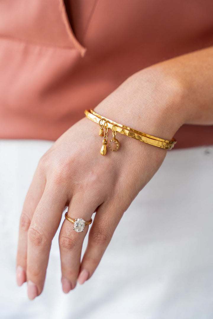 Gold bangle bracelet with peach moonstone, teardrop, and coin charms.