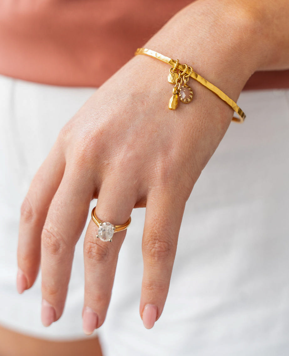 Gold bangle bracelet with peach moonstone, teardrop, and coin charms.