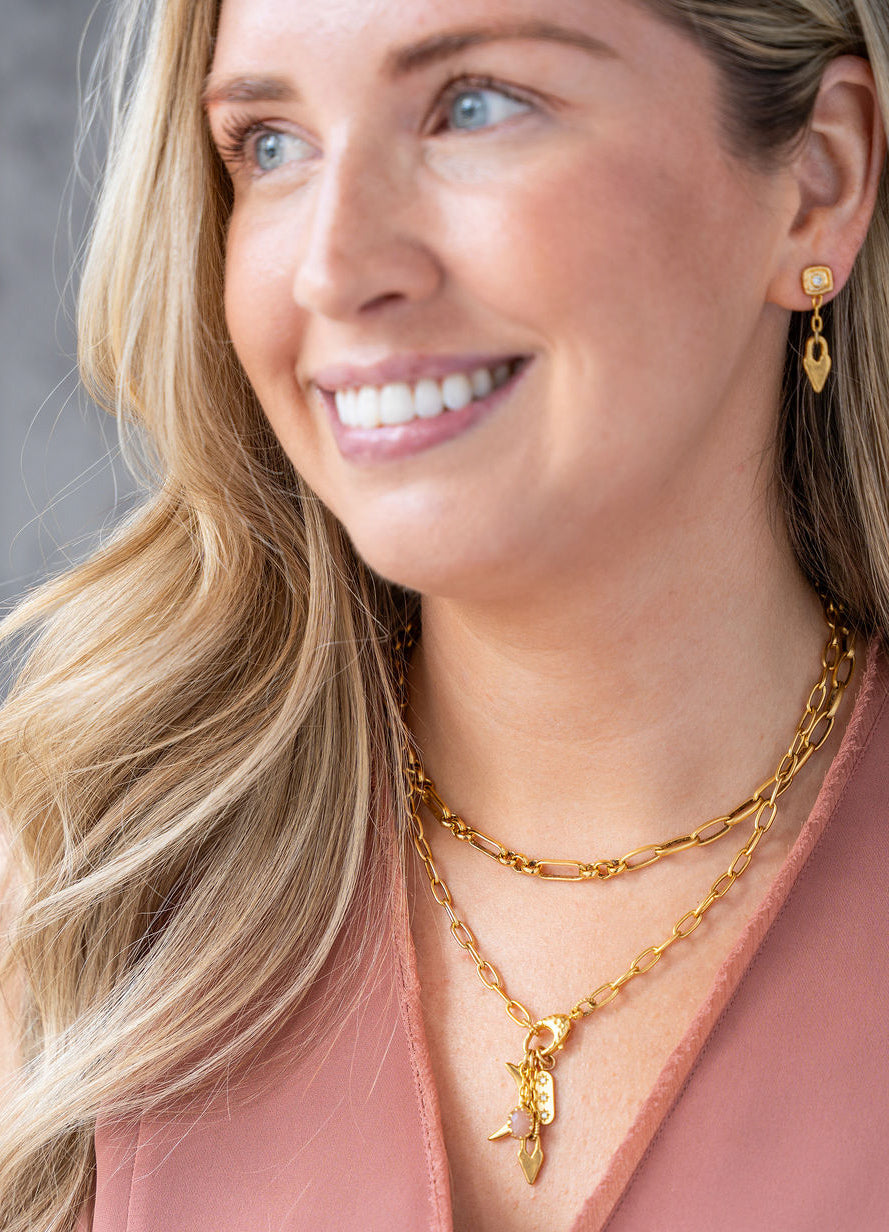 Gold necklace featuring a peach moonstone drop and charm cluster with crescent moon and heart details.