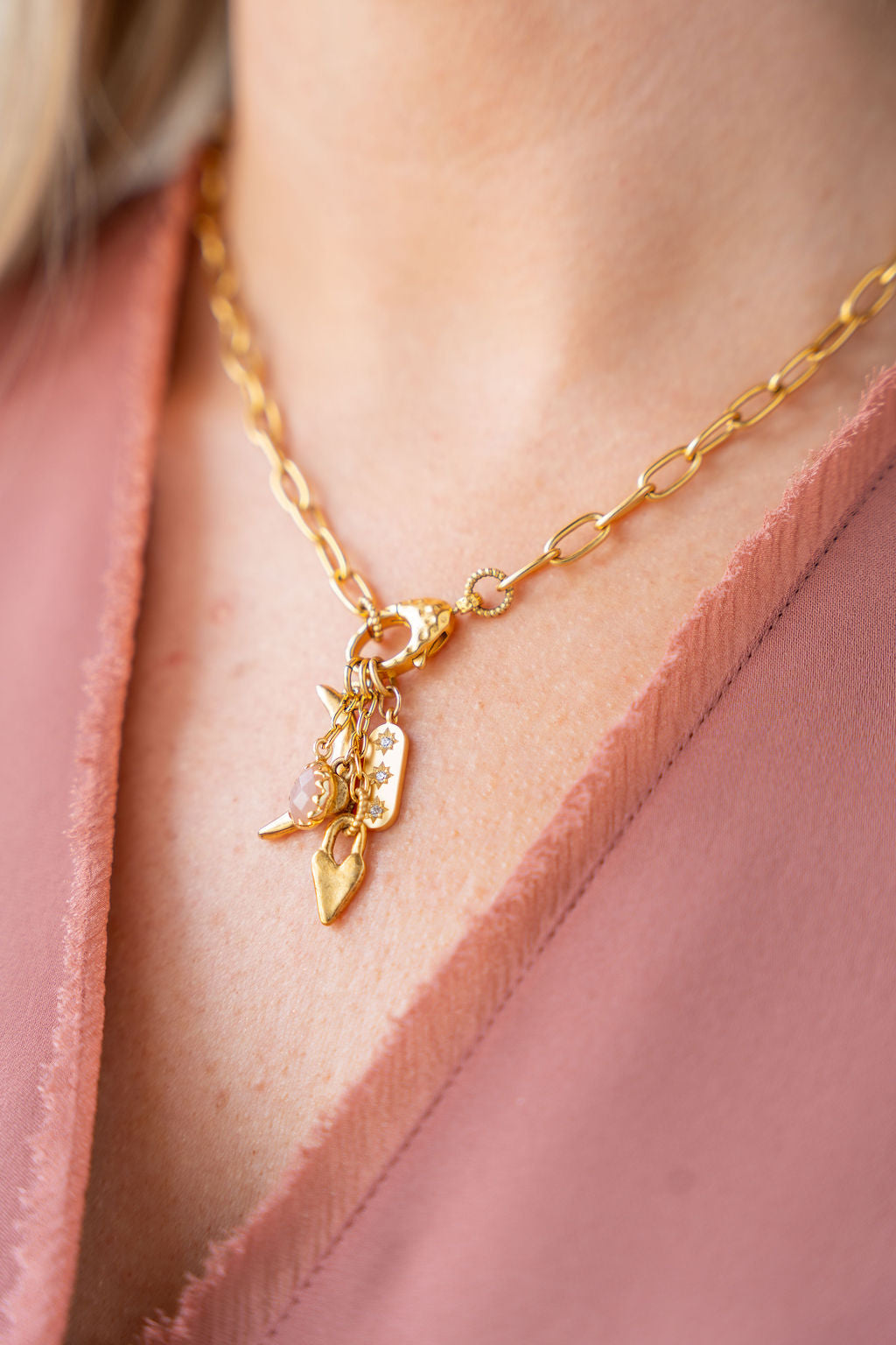 Gold necklace featuring a peach moonstone drop and charm cluster with crescent moon and heart details.