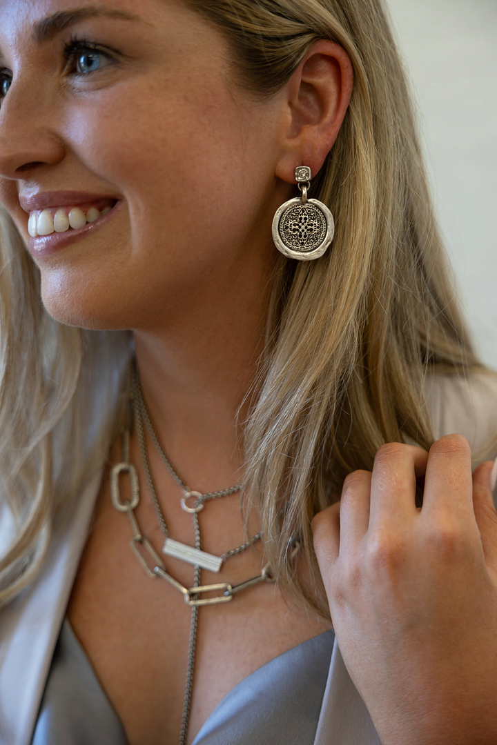 A silver filagree coin dangle earring on a crystal post.