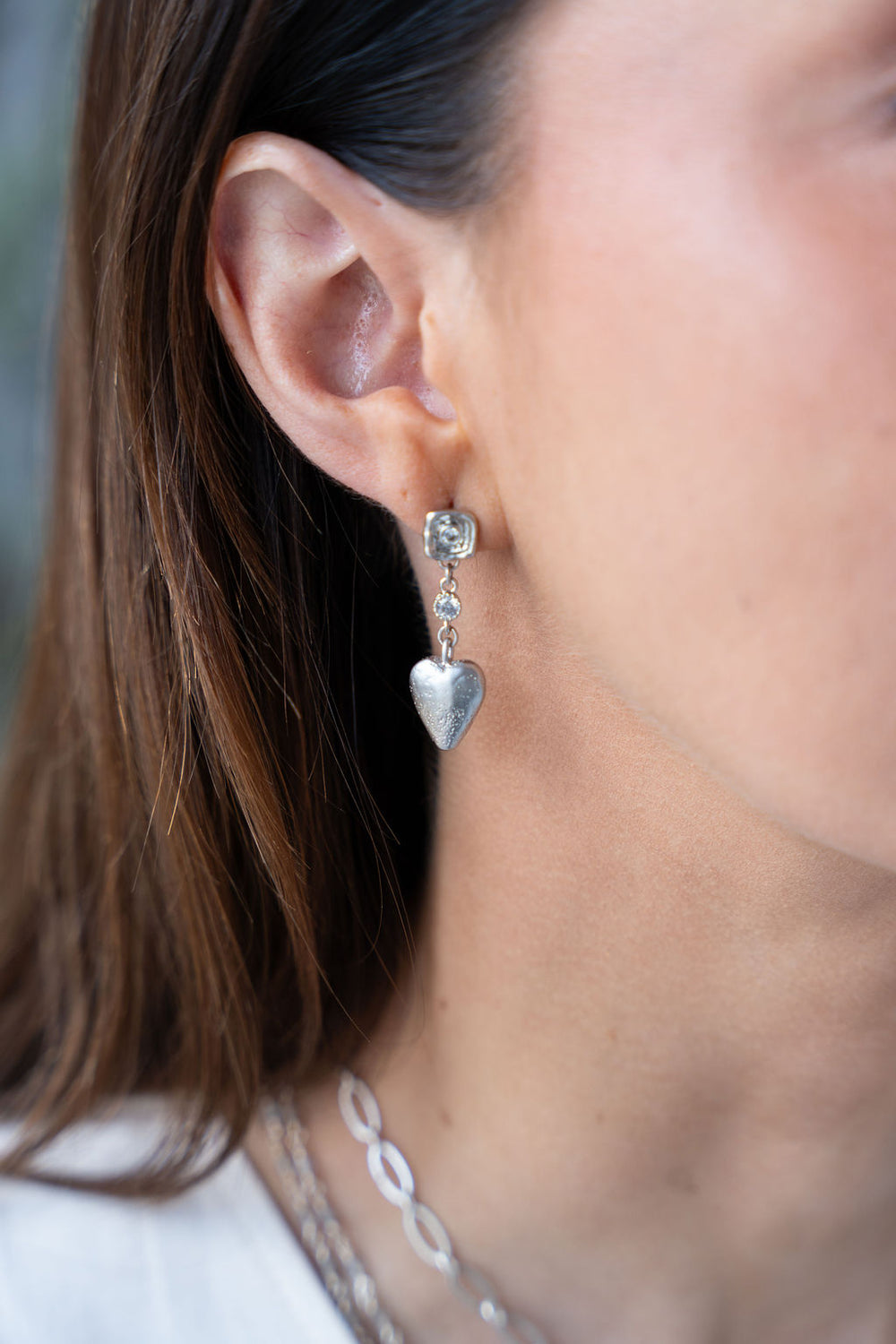 Silver drop earrings with textured puffed hearts and two bezel-set CZ stones on each earring.