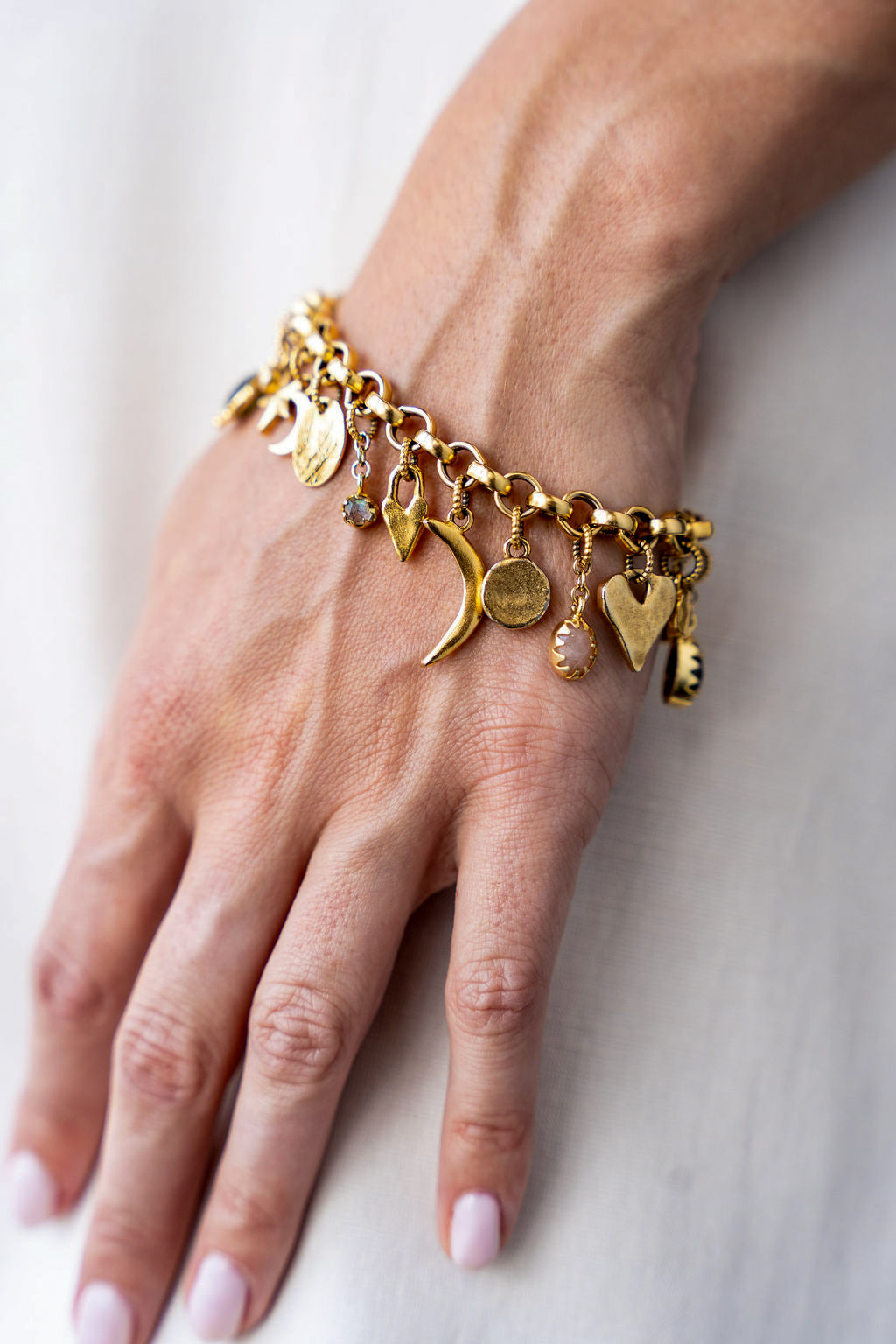 Gold charm bracelet with an eclectic mix of heart, moon, star, and gemstone charms on a chunky chain.