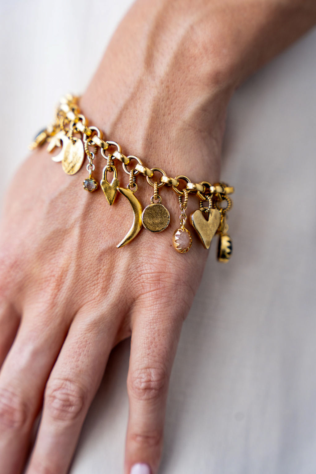 Gold charm bracelet with an eclectic mix of heart, moon, star, and gemstone charms on a chunky chain.
