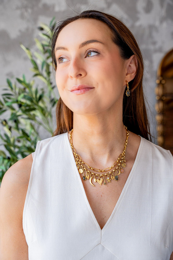 Gold charm necklace with layered chain and assorted symbolic charms including moons, hearts, stars, and gemstones.