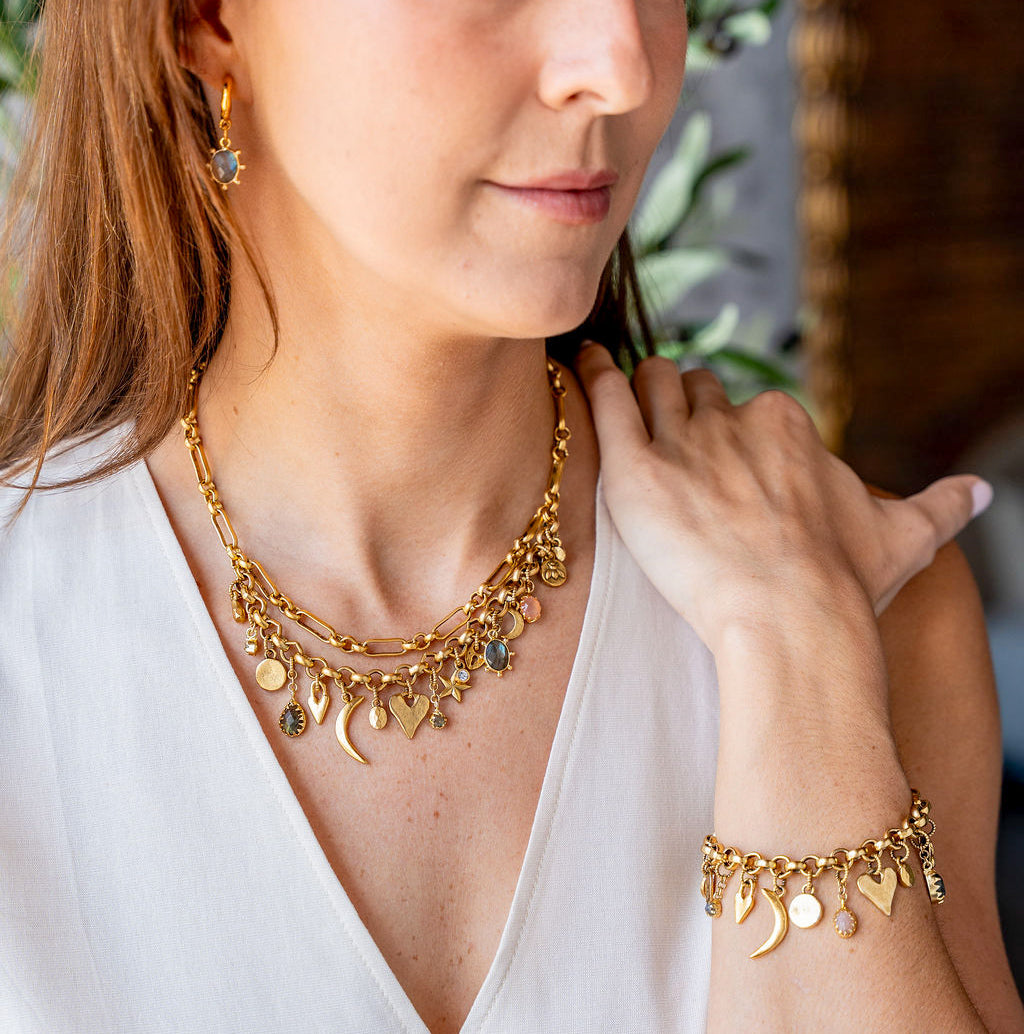 Gold charm necklace with layered chain and assorted symbolic charms including moons, hearts, stars, and gemstones.