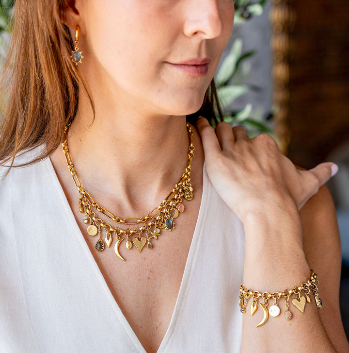 Gold charm necklace with layered chain and assorted symbolic charms including moons, hearts, stars, and gemstones.