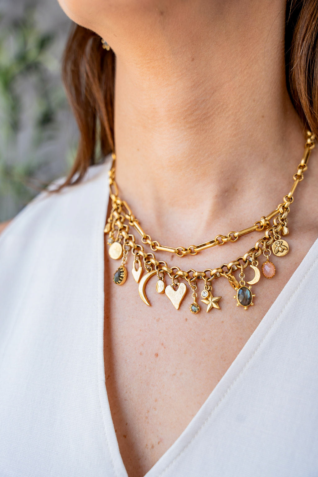 Gold charm necklace with layered chain and assorted symbolic charms including moons, hearts, stars, and gemstones.