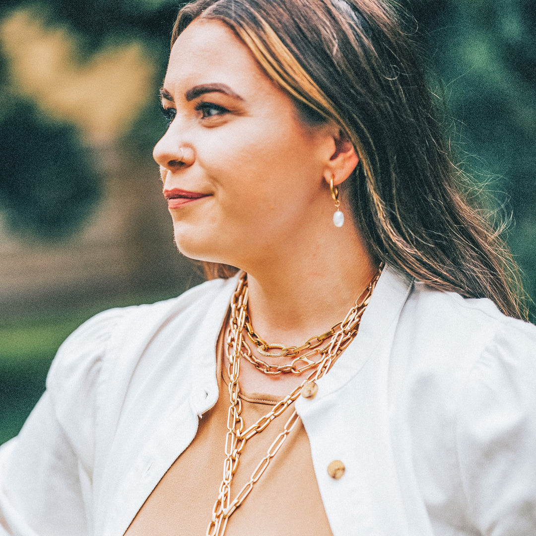 A woman modeling gold chainlink necklaces and pearl earrings.