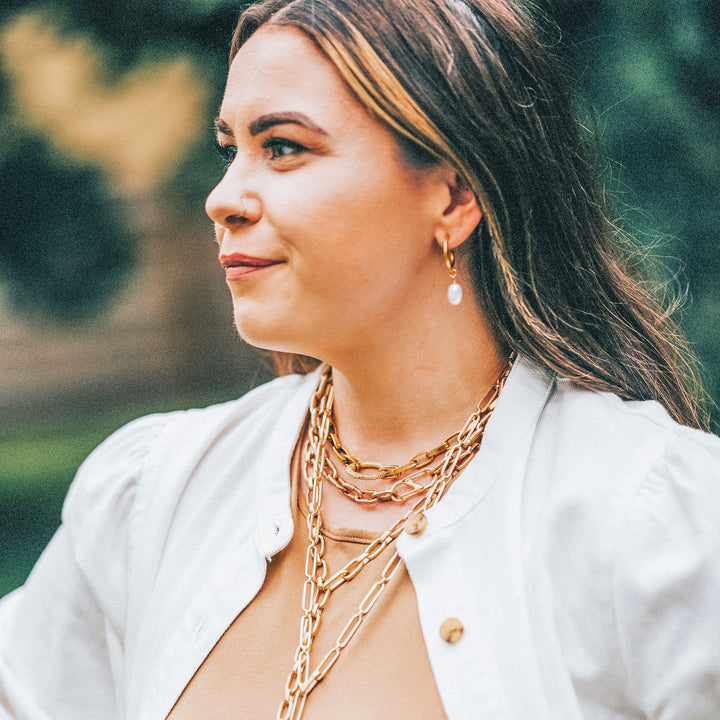 A woman modeling gold chainlink necklaces and pearl earrings.