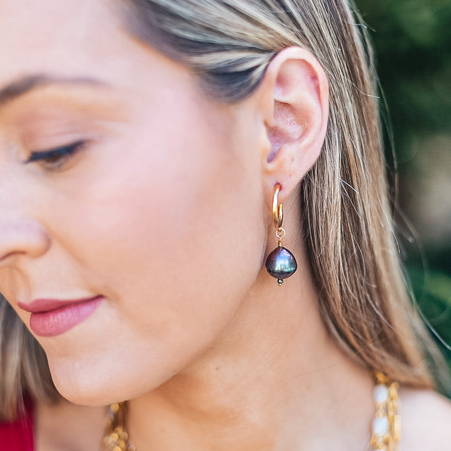 a model wearing a black baroque pearl earring on a gold hoop