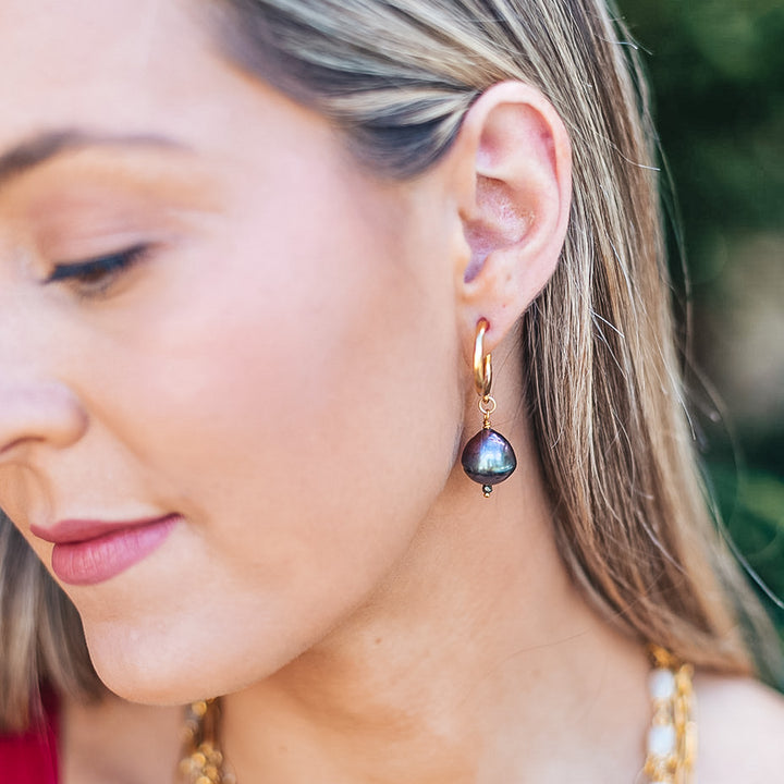 a model wearing a black baroque pearl earring on a gold hoop