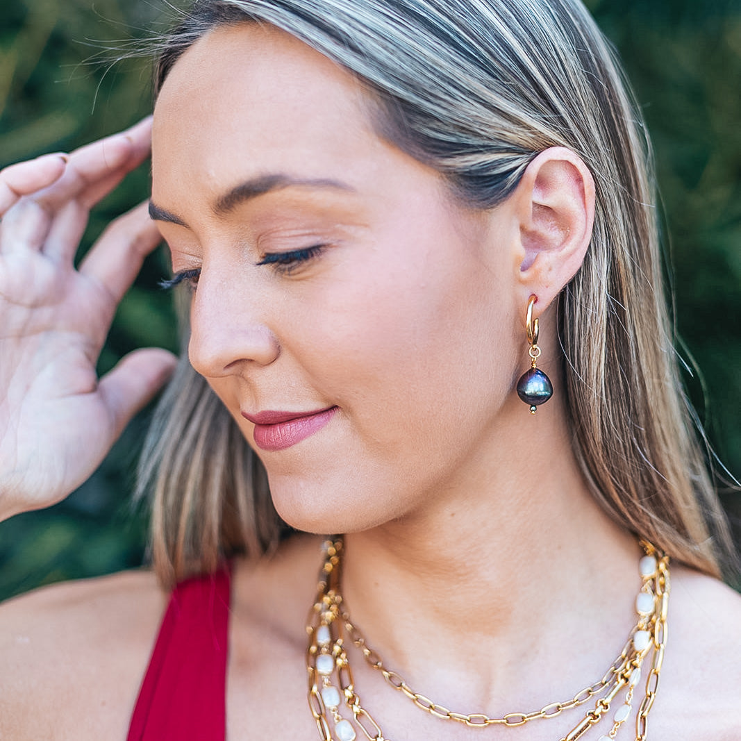 a model wearing a black baroque pearl earring on a gold hoop