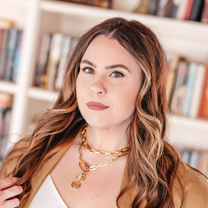 A model wearing gold layered chainlink necklaces with fireworks, hamsa, and star charms on a snap clasp.