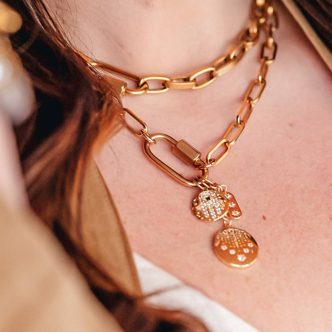 A model wearing gold layered chainlink necklaces with fireworks, hamsa, and star charms on a snap clasp.
