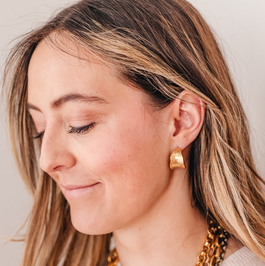 A model wearing matte gold post hoop earrings.