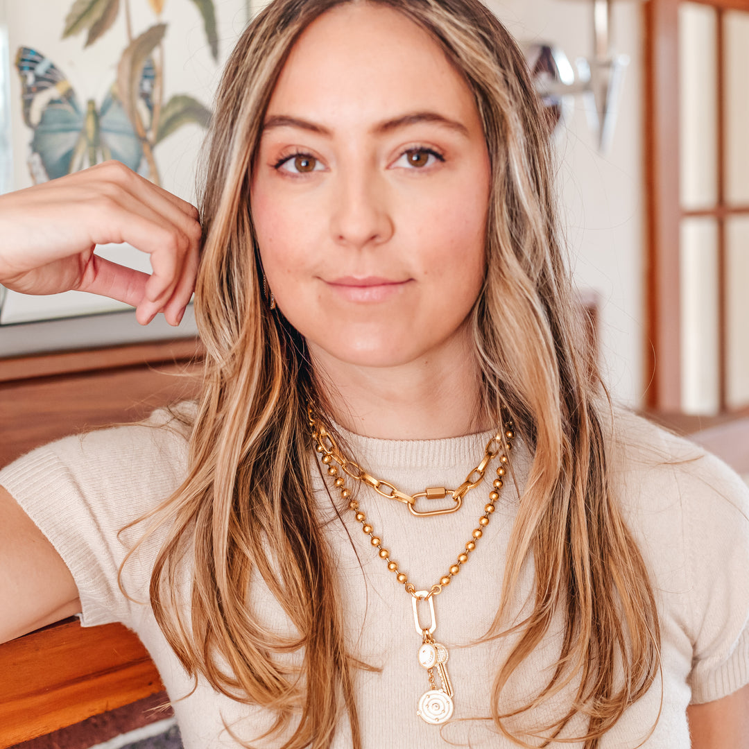 A model wearing layered gold chainlink necklaces with charms.