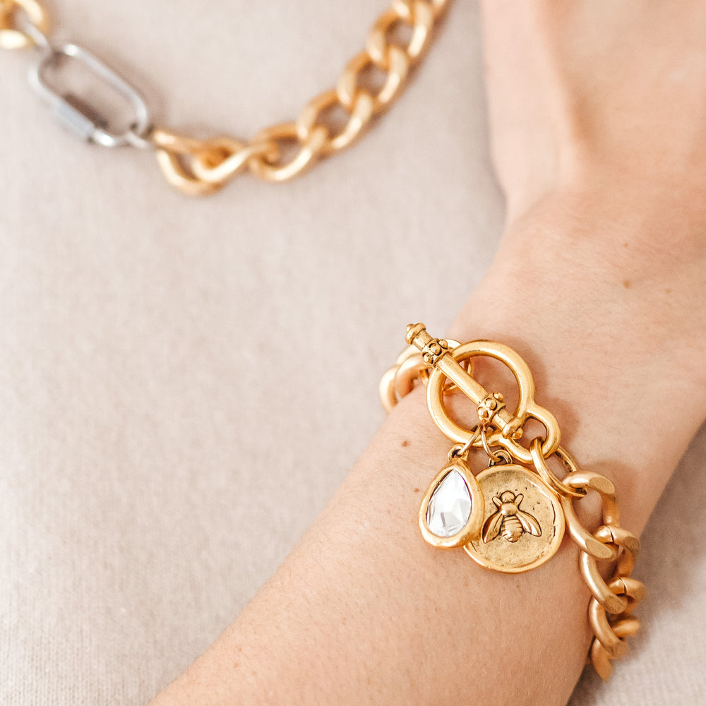 A woman's wrist modeling gold chainlink bracelets with bee and crystal charms.