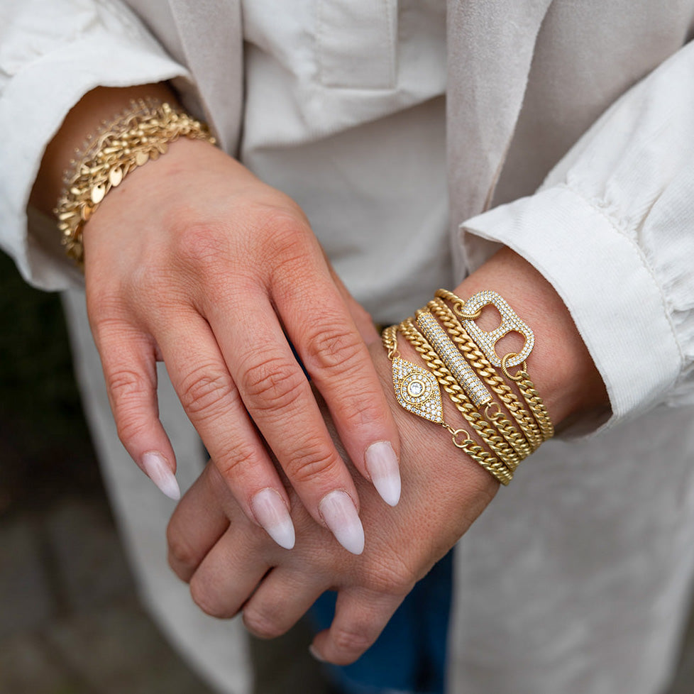 a matte gold pave bracelet stack with evil eye, can tab and pave bar details.