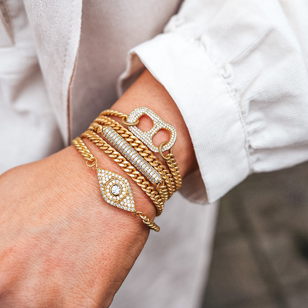 a matte gold pave bracelet stack with evil eye, can tab and pave bar details.