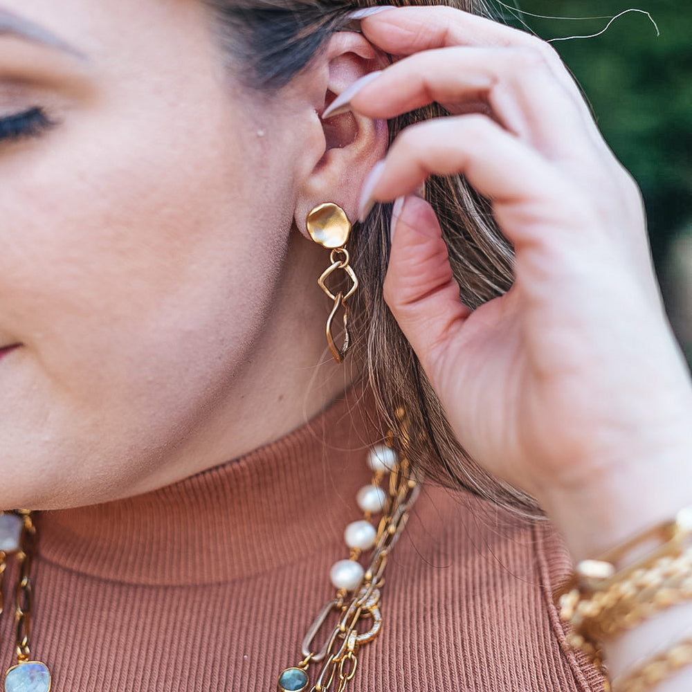 a model wearing a nested square matte gold earring on a lotus leaf post