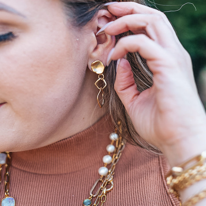 a model wearing a nested square matte gold earring on a lotus leaf post