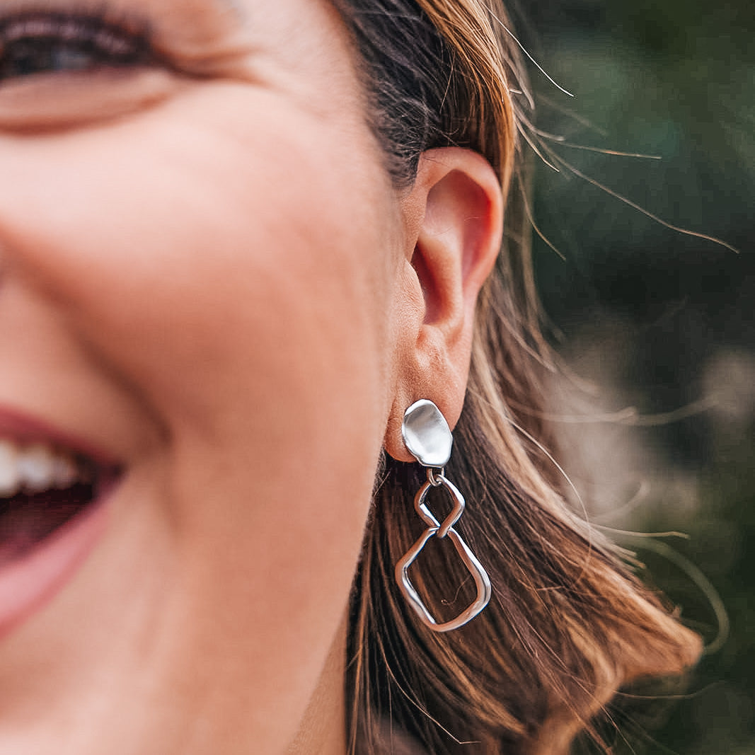 A matte silver dangle earring with nested square detail on a lotus leaf post.