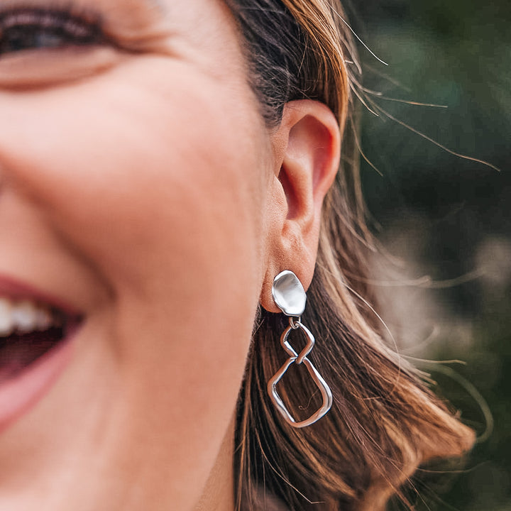 A matte silver dangle earring with nested square detail on a lotus leaf post.