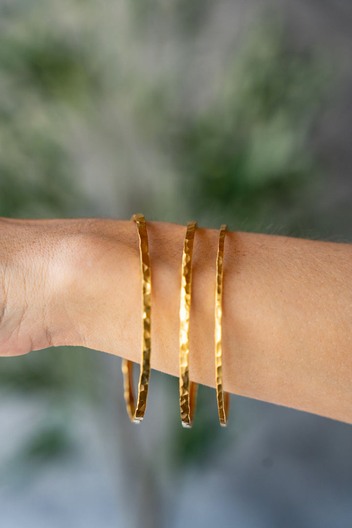 Wide hammered gold bangle bracelet with organic hand-forged texture.