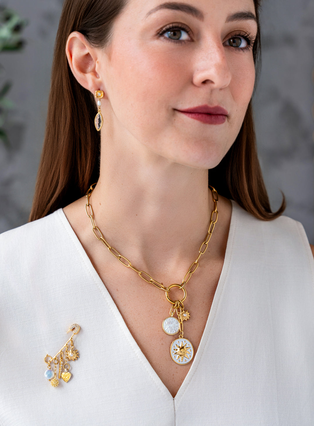 Gold celestial brooch pin with dangling pearl, crystal pavé charm, heart pendant, textured orb, and sunburst charm.