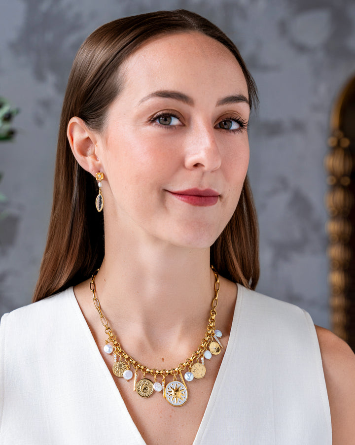Gold celestial charm necklace with sun medallions, coin pearls, pavé crystal accents, and dangling celestial charms on a chunky chain.