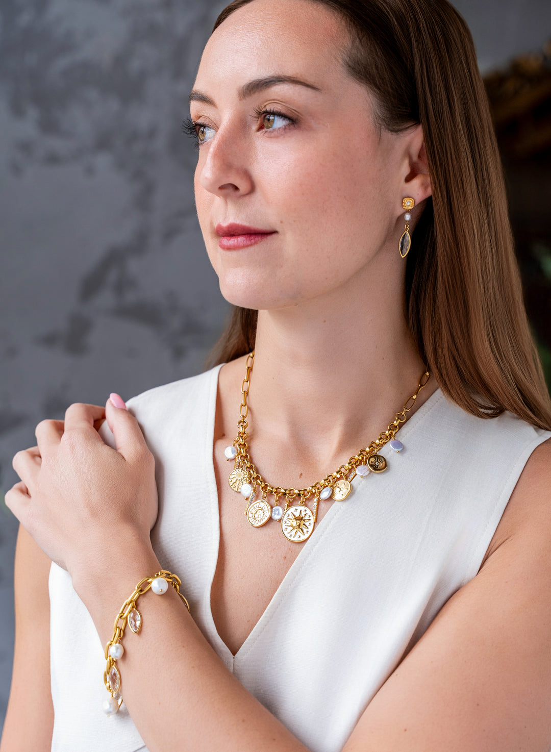 Gold celestial charm necklace with sun medallions, coin pearls, pavé crystal accents, and dangling celestial charms on a chunky chain.