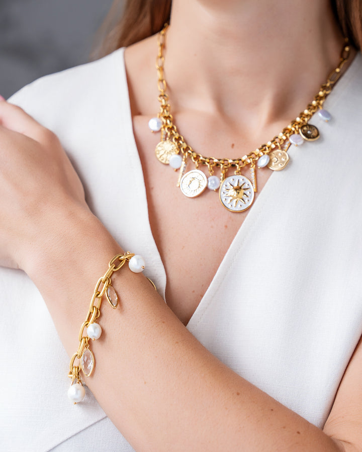 Gold celestial charm necklace with sun medallions, coin pearls, pavé crystal accents, and dangling celestial charms on a chunky chain.
