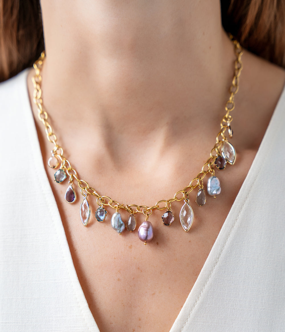 Gold charm necklace with colorful faceted gemstone charms and freshwater pearls dangling from an elongated gold chain.