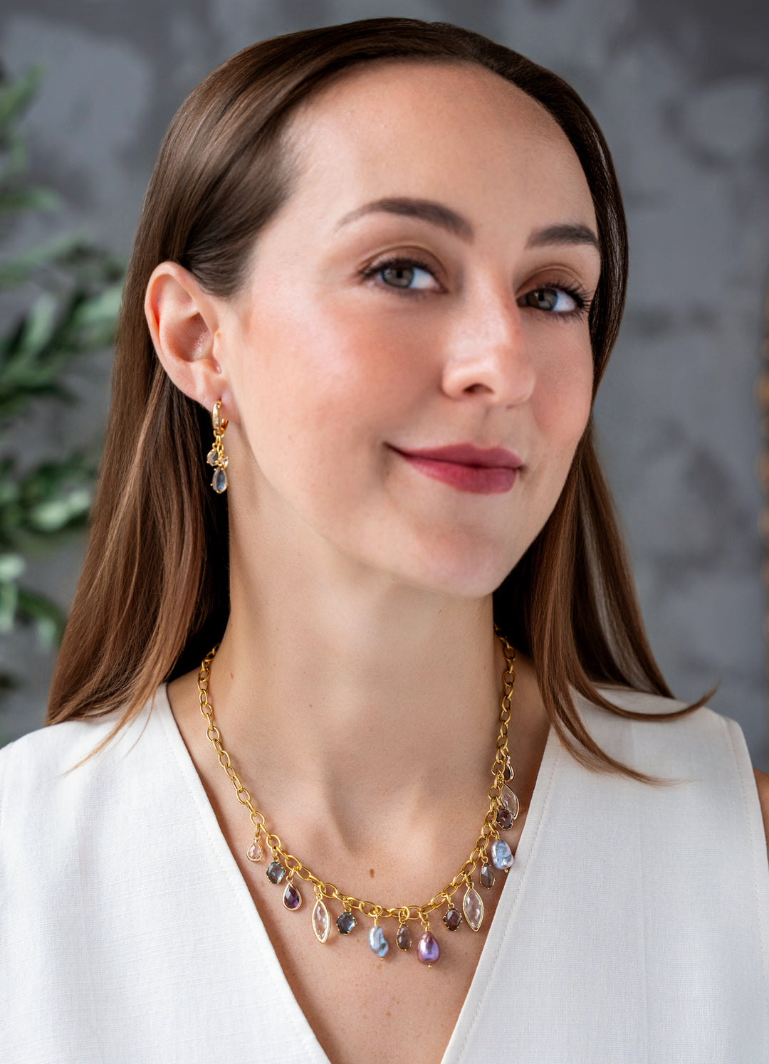 Gold charm necklace with colorful faceted gemstone charms and freshwater pearls dangling from an elongated gold chain.