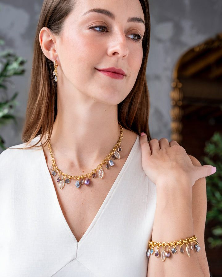 Gold charm necklace with colorful faceted gemstone charms and freshwater pearls dangling from an elongated gold chain.