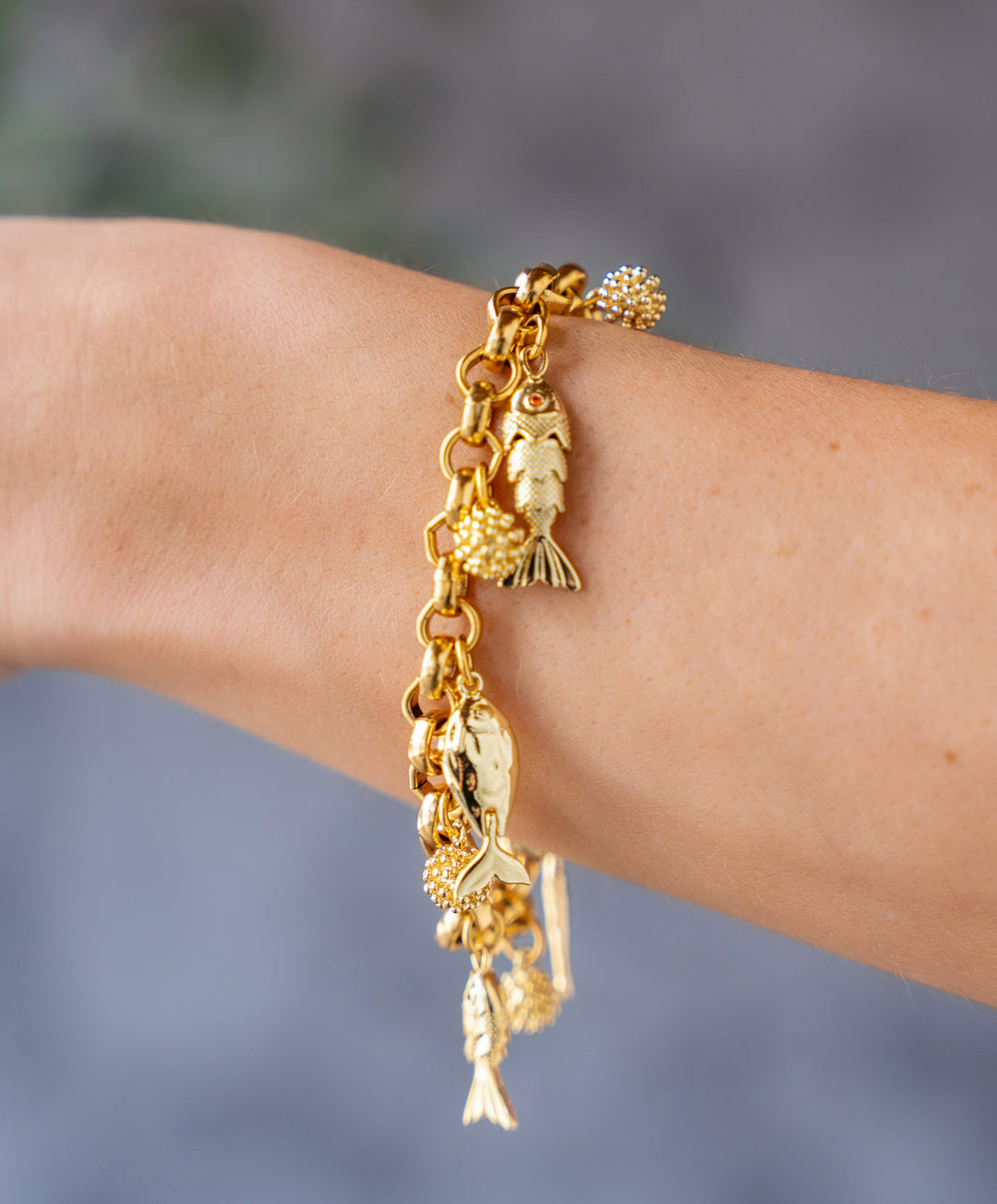 Gold charm bracelet with dangling fish charms and textured gold bead accents on a chunky chain.